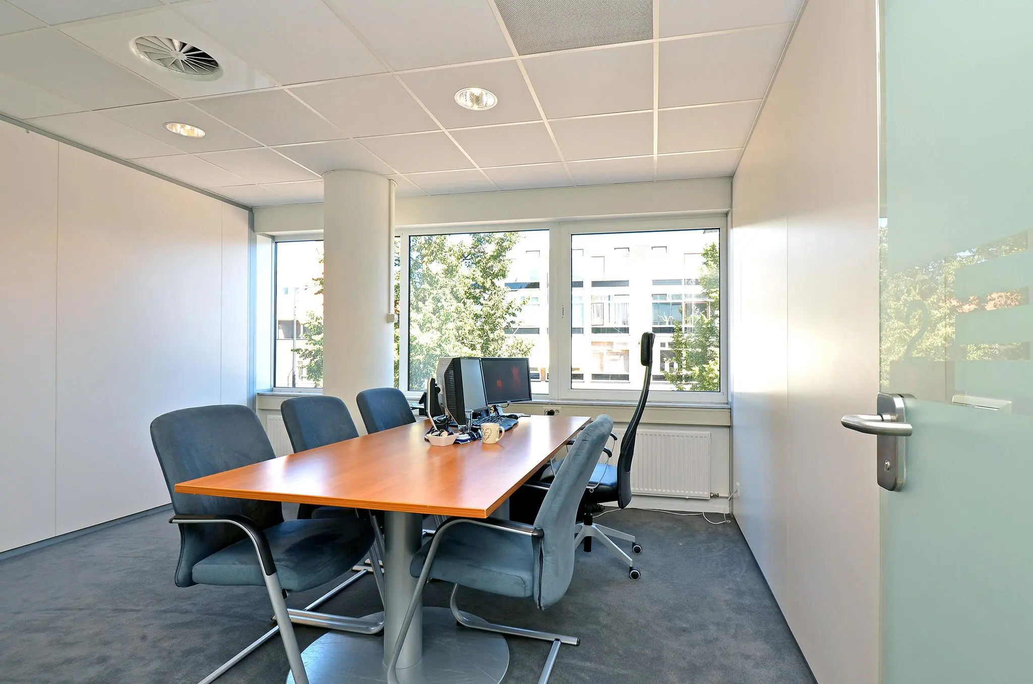 Vergaderruimte met een houten tafel, zes stoelen en computers, gelegen aan de 1e Hogeweg.